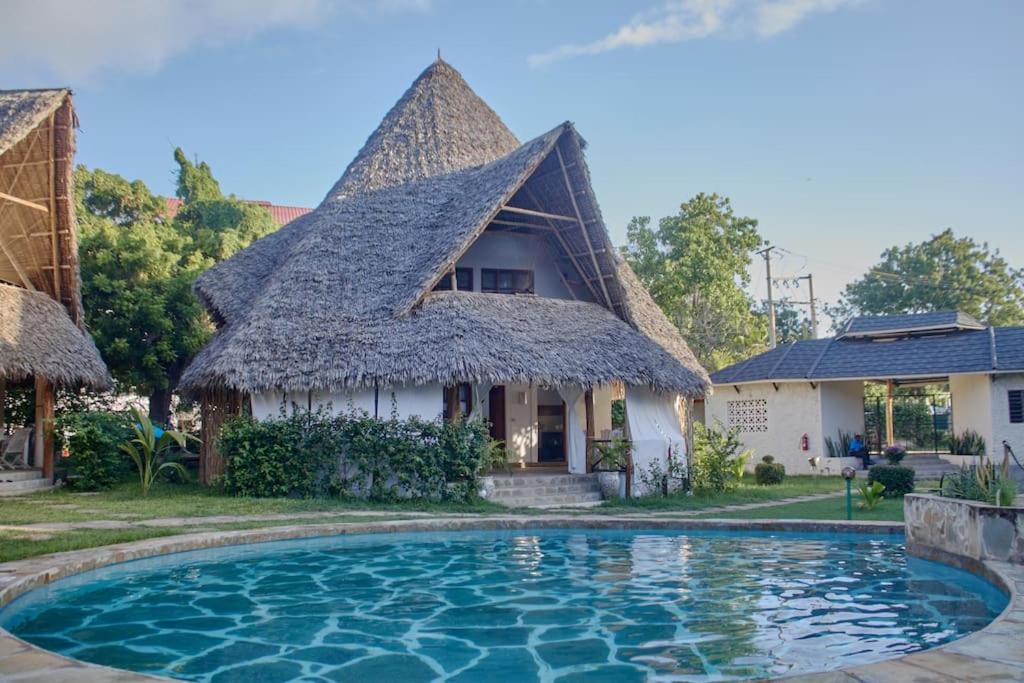 a house with a thatched roof and a swimming pool at Cosy Cottage Marine Park - 2 Rooms in Malindi