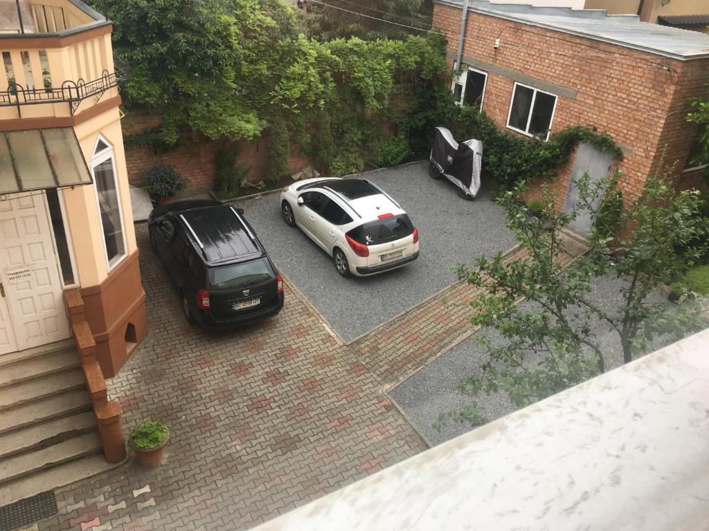 dos autos estacionados en un estacionamiento frente a una casa en Номера та Паркінг- Rooms & Parking, en Chernivtsi