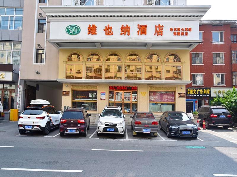 un gruppo di auto parcheggiate di fronte a un edificio di Vienna Hotel Harbin Train Station Jianguo Street a Harbin