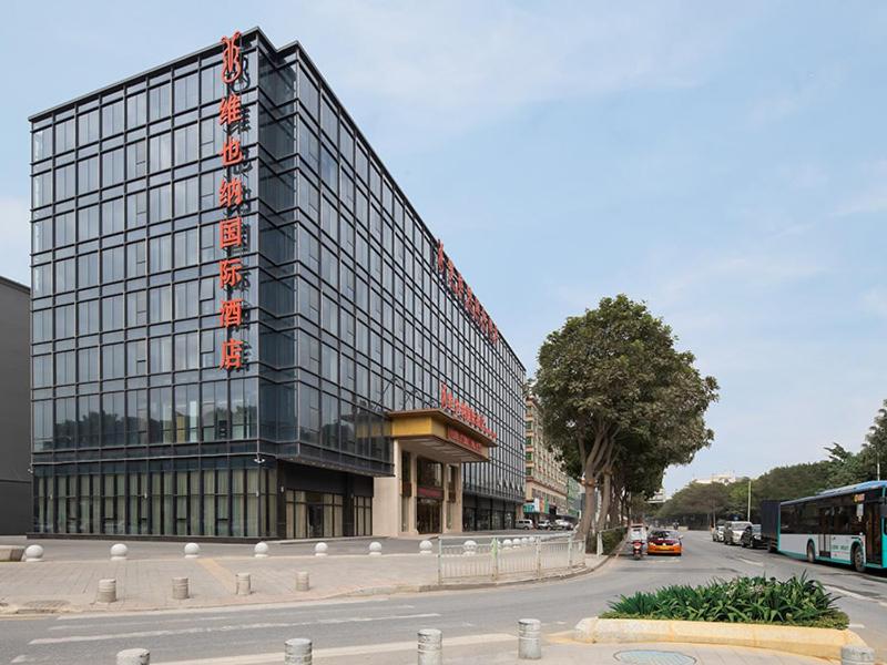 a large glass building on the side of a street at Vienna International Hotel South Gate of Shenzhen International Convention and Exhibition Center in Bao'an