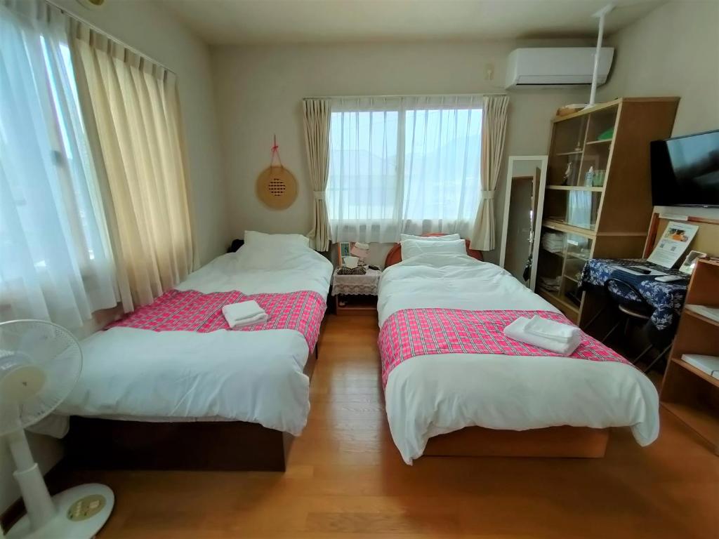 a bedroom with two beds and a tv and a window at 民泊マエダハウス B&B Maeda House in Aira