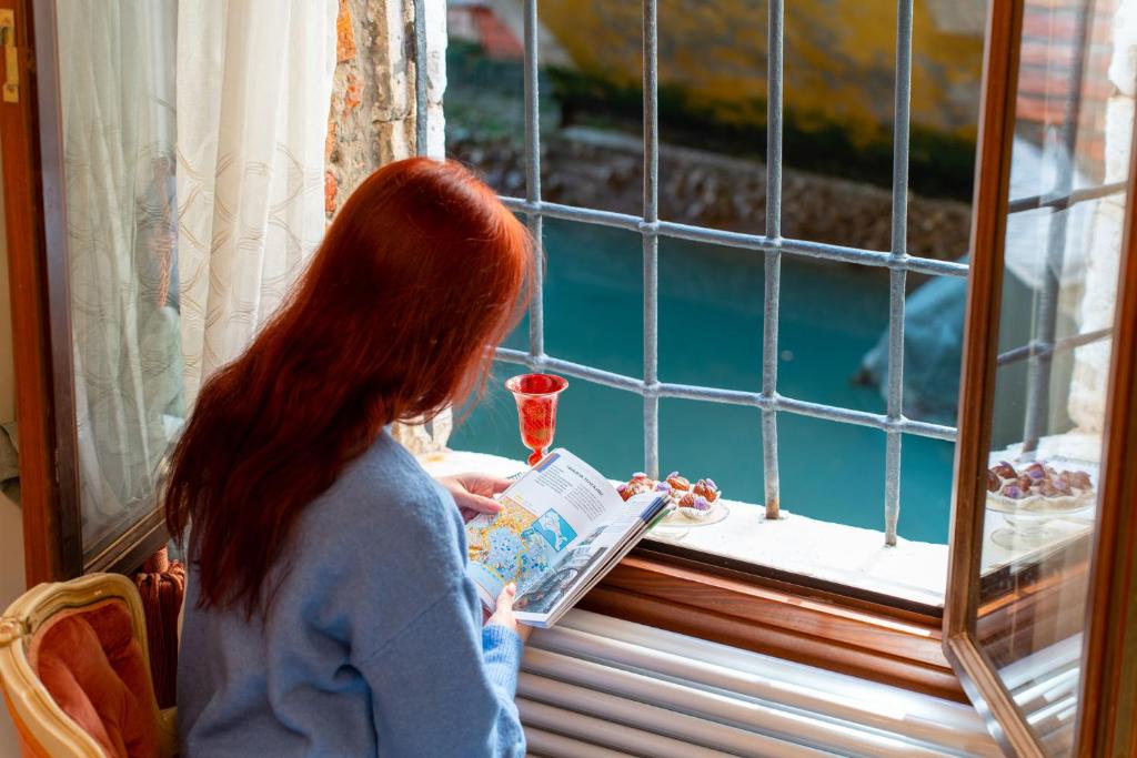 uma mulher a ler um livro em frente a uma janela em Casa al Ponte Scudi - 4 Windows on the Canal em Veneza