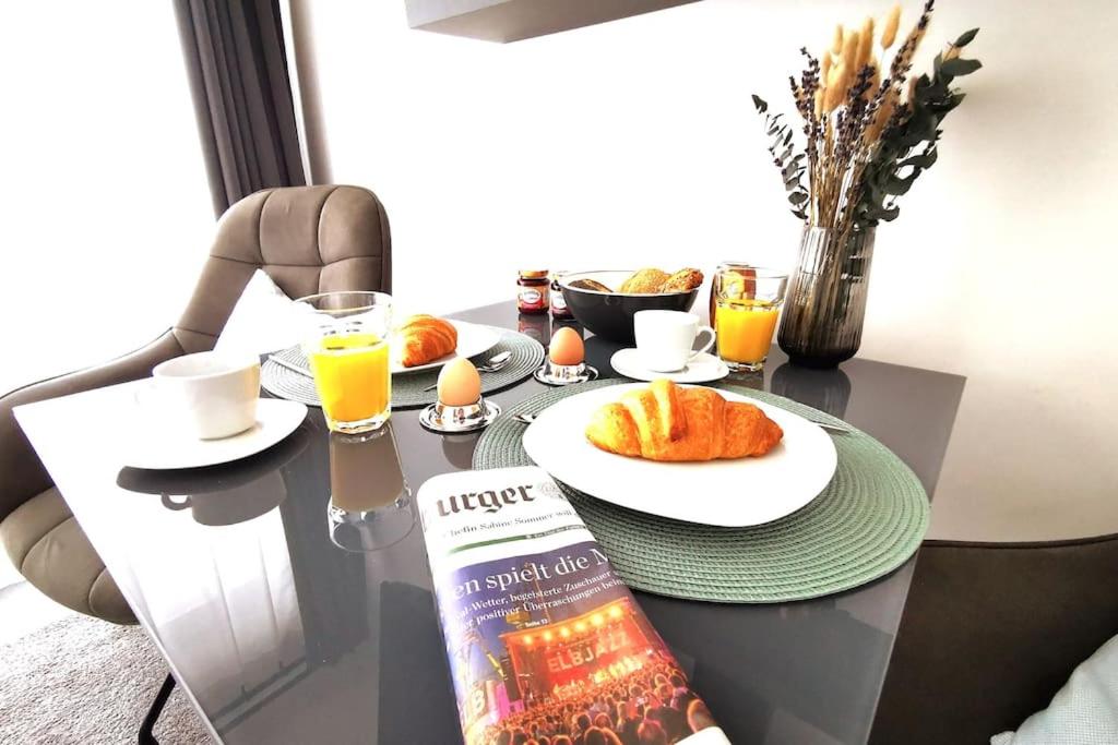 a table with a breakfast of orange juice and croissants at Hamburg 04 Modernes Apartment am Winterhuder Marktplatz Alster Stadtpark in Hamburg