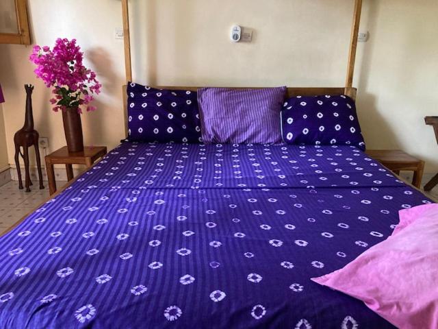 a blue bed with purple sheets and purple pillows at Villa Rose in Bobo-Dioulasso