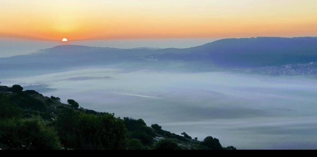 a misty sunrise with the sun rising over the mountains at בית אירוח אישי/זוגי ומשפחתי בגליל התחתון אבטליון in Avtalyon