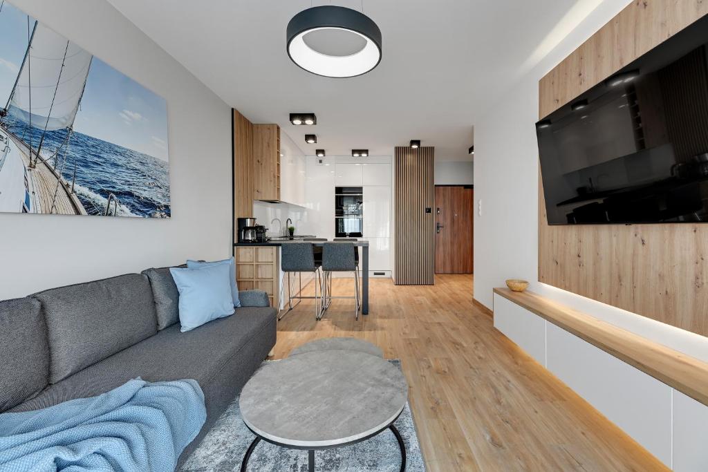 a living room with a gray couch and a kitchen at Downtown Apartments Seaside Baltea Park & Parking in Gdańsk