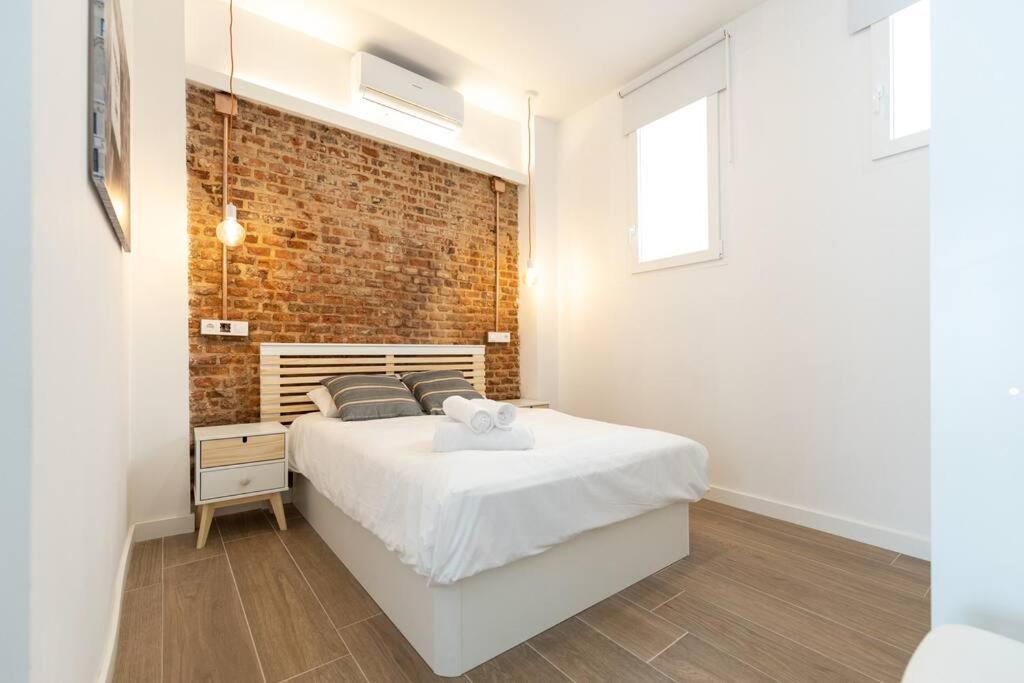 een slaapkamer met een wit bed en een bakstenen muur bij Apartamento 1hab con estilo cerca de Ventas in Madrid