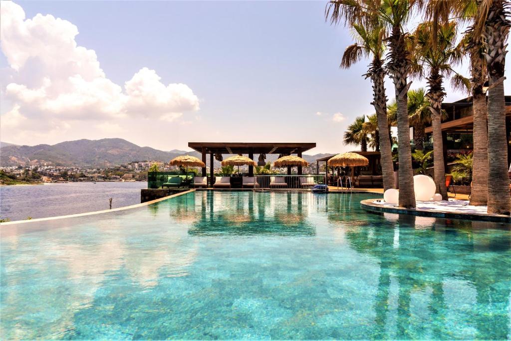 einen Pool mit Palmen und Blick auf das Wasser in der Unterkunft Ala Suites and Villas Yalıkavak in Yalıkavak