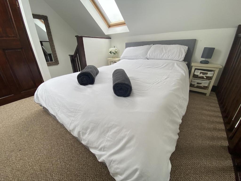 1 dormitorio con 1 cama con sábanas blancas y zapatillas negras en The Stables - Detached Cottage with Private Garden & Hot Tub, en St Austell