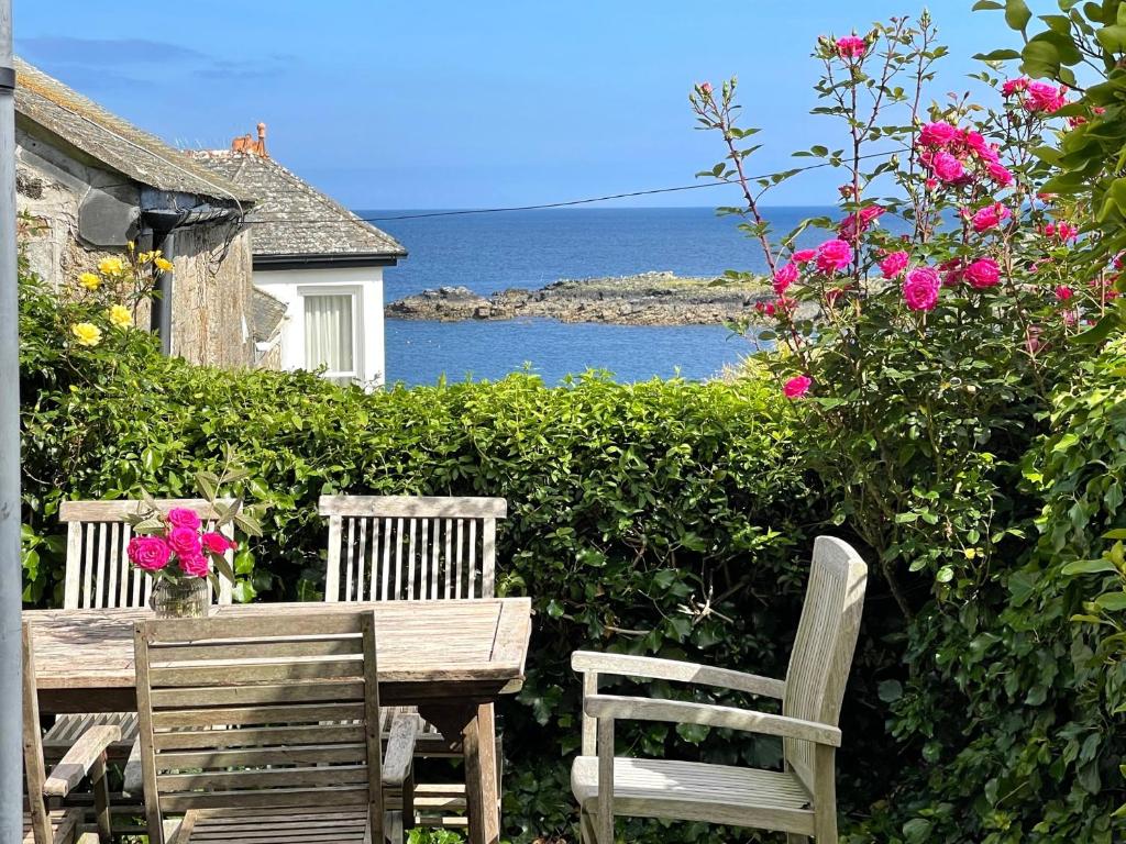 due sedie e un tavolo in legno con fiori e l'oceano di Mousehole Cottage a Penzance