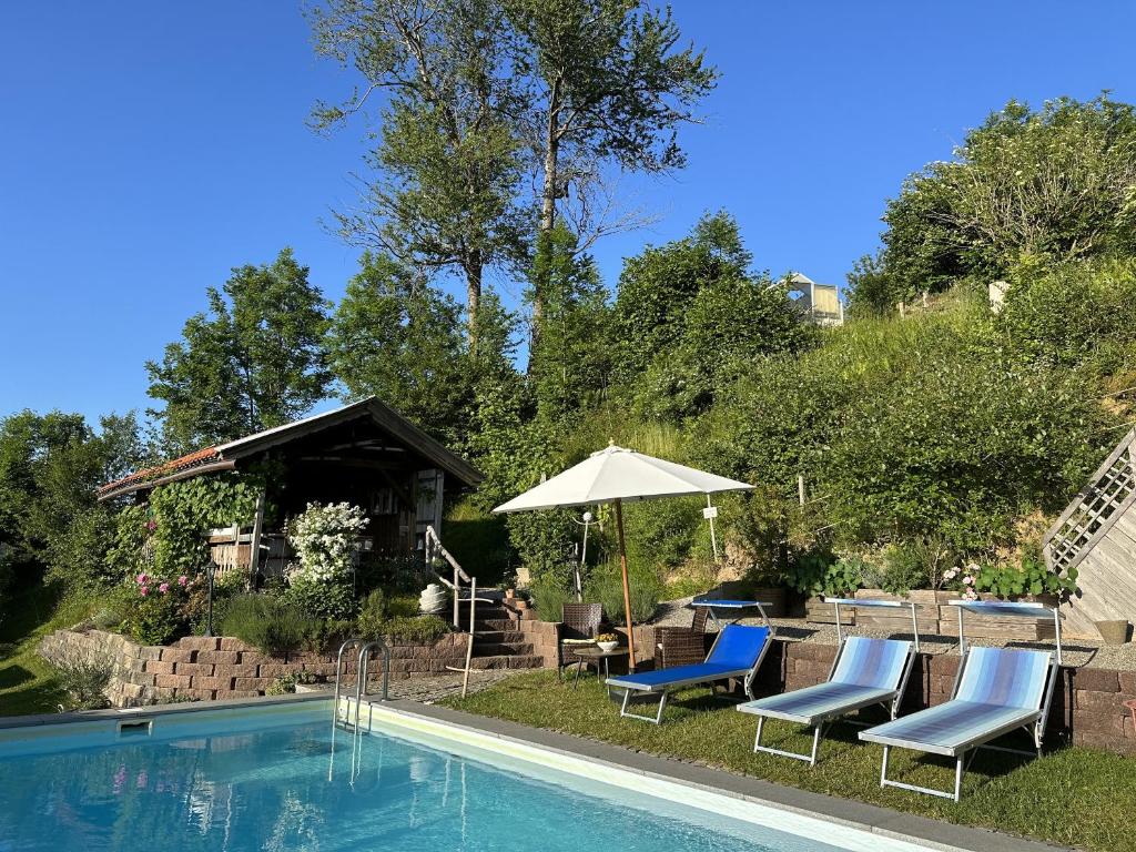 uma piscina com cadeiras e um guarda-sol ao lado em Ferienwohnung Oberberg em Oberreute