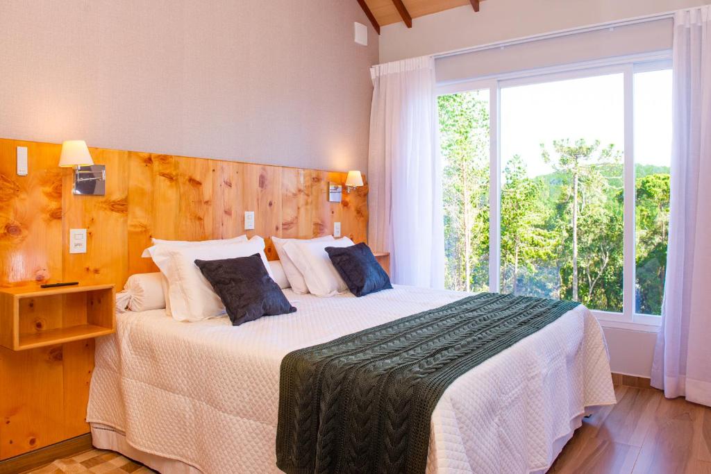 a bedroom with a large bed with a large window at Timber Lodge Camanducaia in Monte Verde