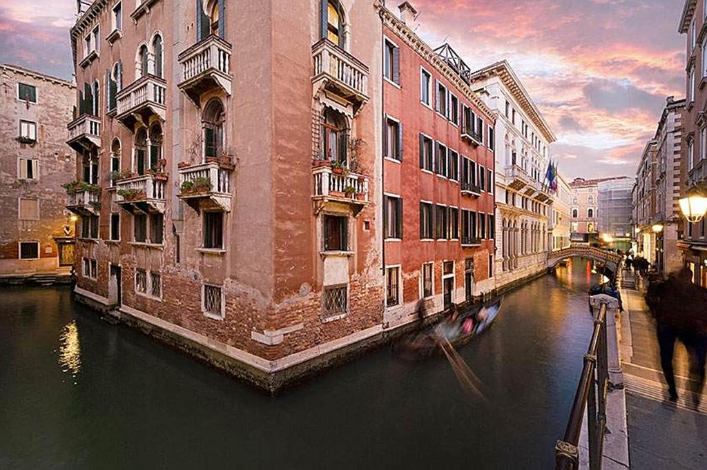 a canal in a city with buildings and a boat at Palazzo Orseolo- Gondola View in Venice