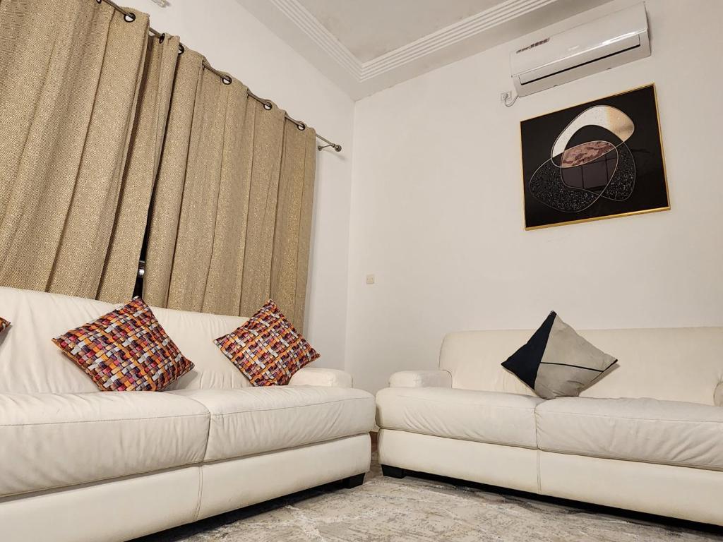 una sala de estar con 2 sofás blancos y cortinas en KADIDJA APARTMENTS & SUITES Hedzranawoe, en Lomé