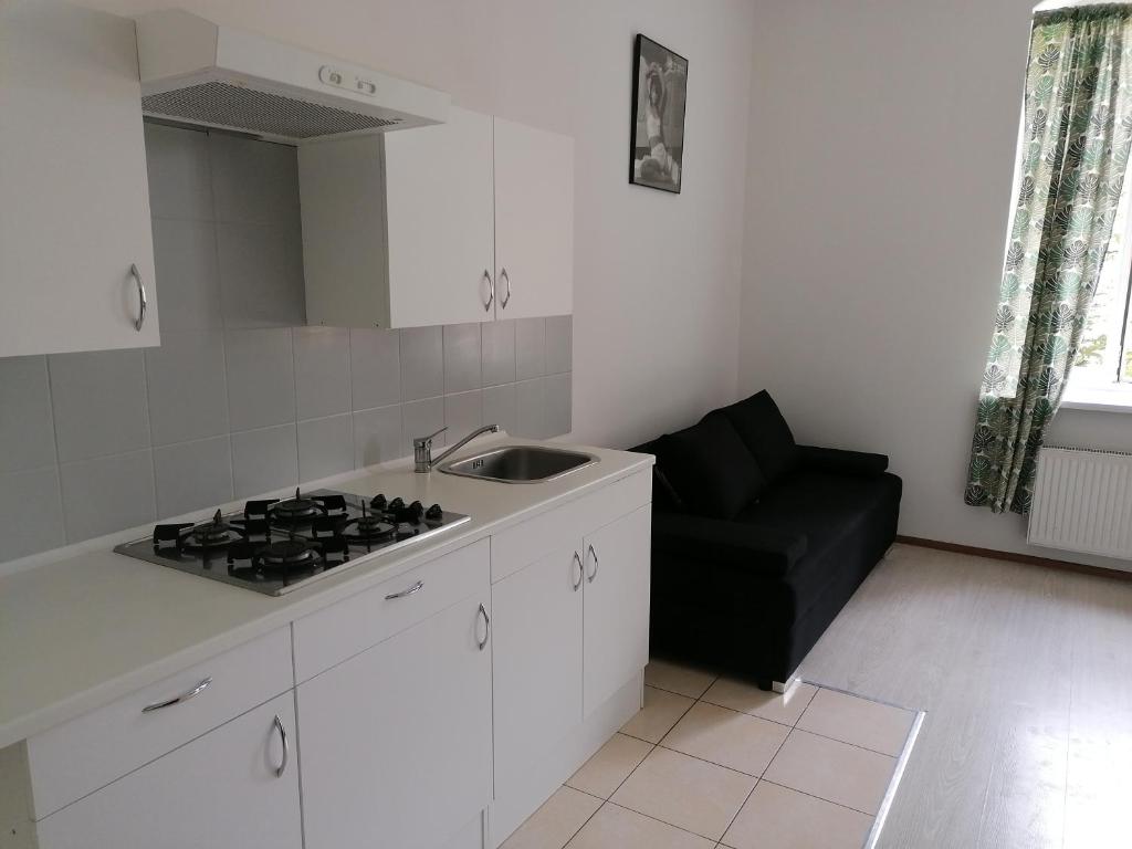 a kitchen with a stove and a black couch at Przytulne Mieszkanko Centrum in Mrągowo