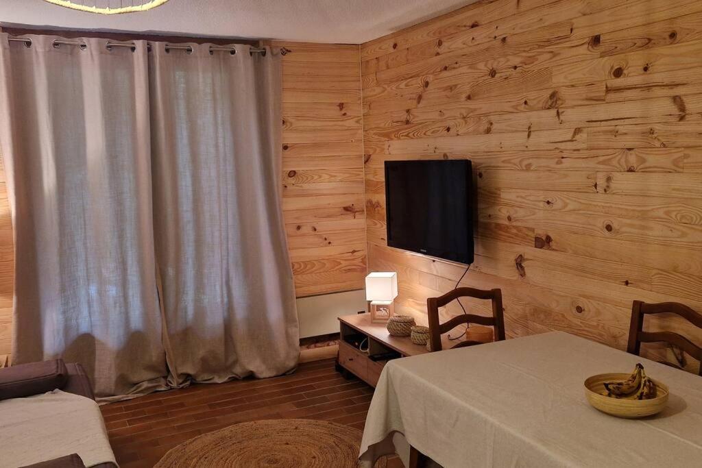 uma sala de estar com uma mesa e uma televisão na parede em Appartement 3 pièces avec jardin em Valdeblore