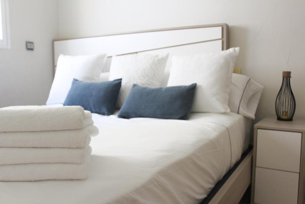 Cama blanca con sábanas blancas y almohadas azules en Apartamento Bahía, en Santa Pola