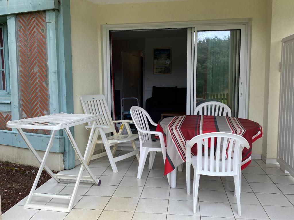 une terrasse couverte avec des chaises blanches, une table, une table et des chaises dans l'établissement Apt T2 sur Golf Moliets et Maa, à Moliets-et-Maa