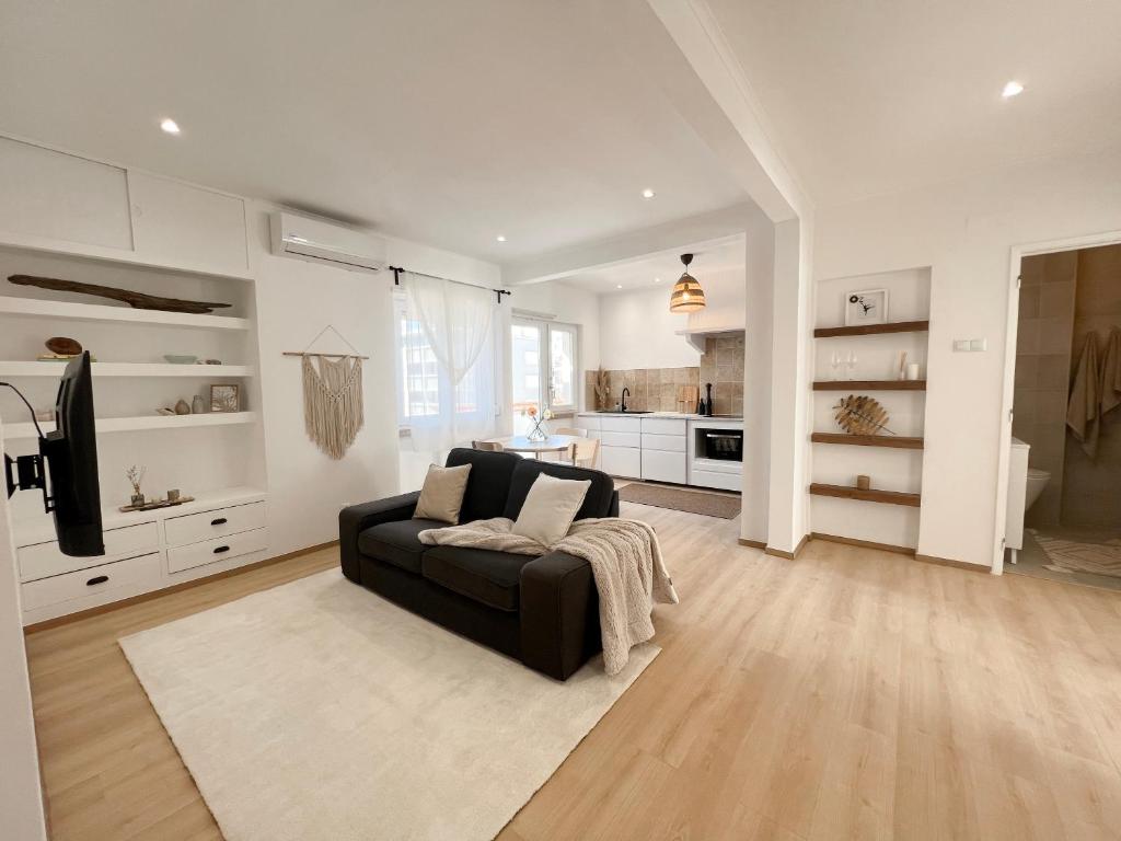 a living room with a black couch and a kitchen at Capitão Ribeiro Surf House in Costa da Caparica