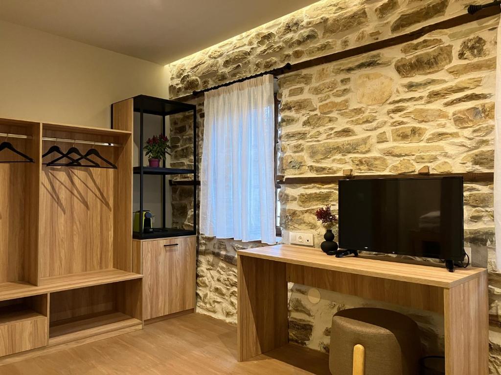 a living room with a tv and a stone wall at Melofegaro Guesthouse in Palaios Panteleimonas