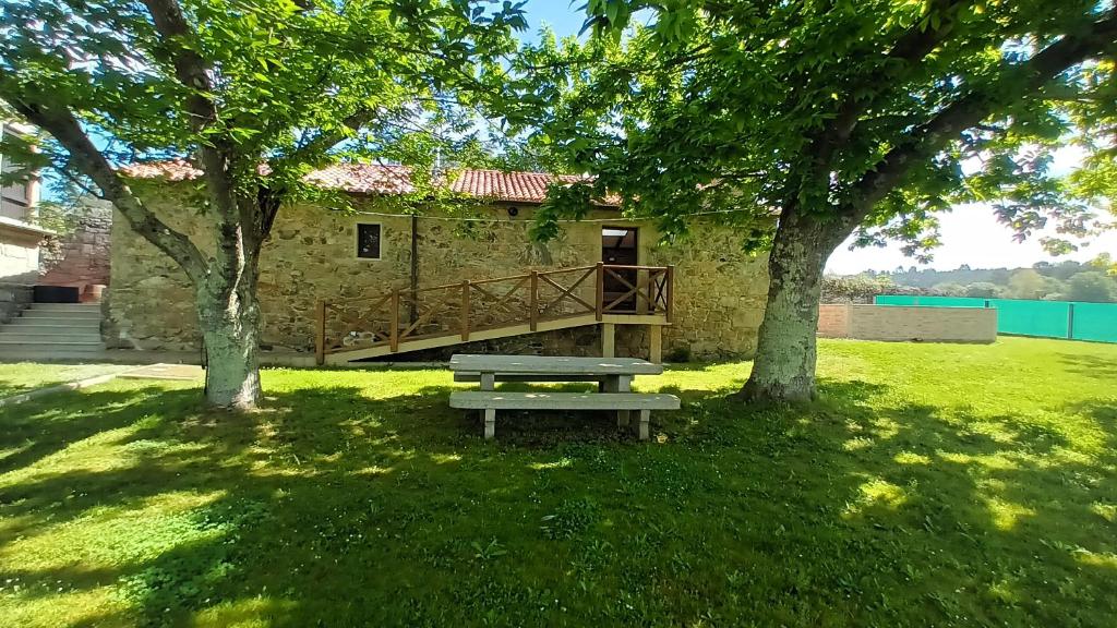 einen Picknicktisch auf einem Feld mit Bäumen und einem Gebäude in der Unterkunft A caseta de Mourelle in Amés