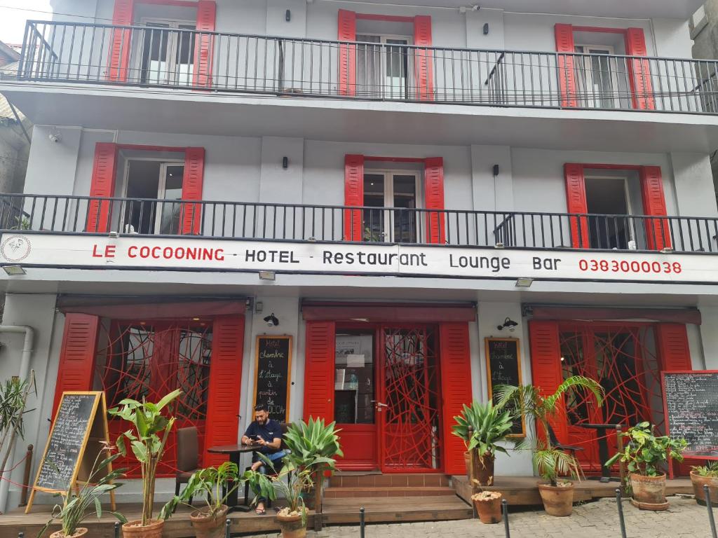 un homme est assis devant un bâtiment rouge dans l'établissement Le Cocooning 974 Hôtel Restaurant Réunion, à Antananarivo