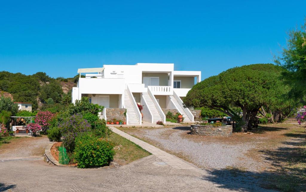 a white house on a hill with trees and bushes at Tselios Apartments & Studios in Kiotari