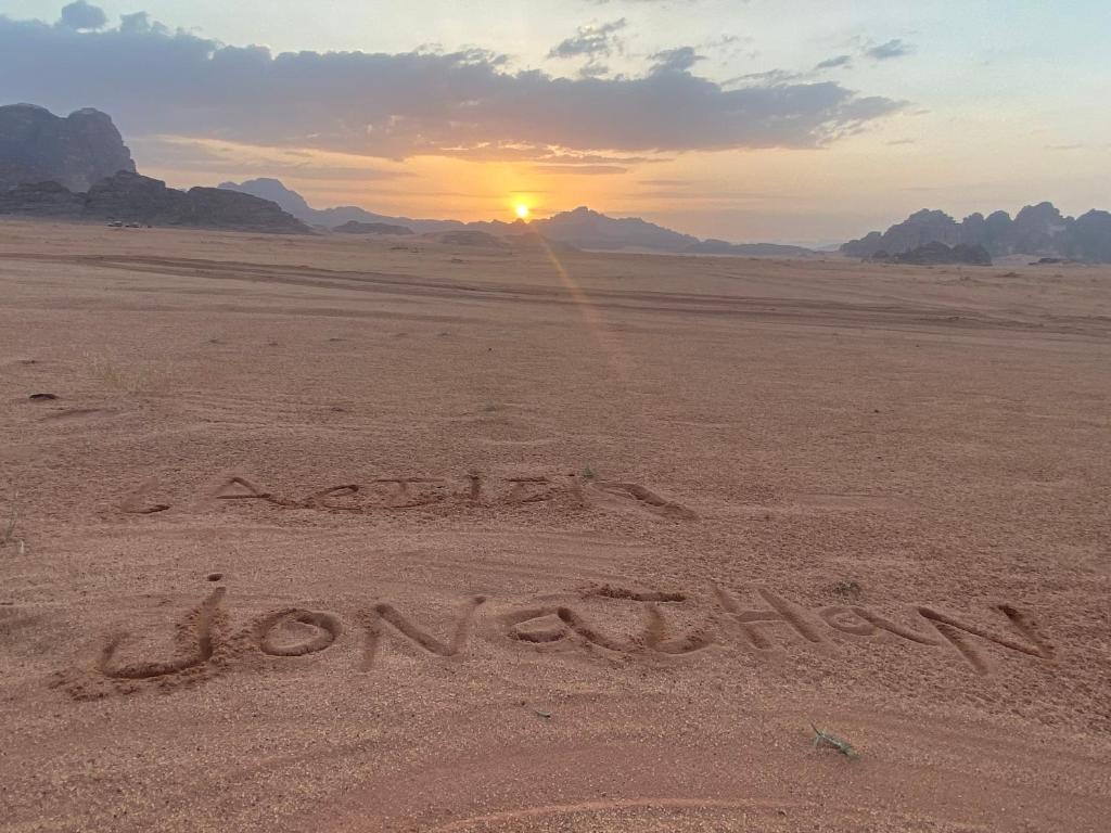een inscriptie in de woestijn met de zonsondergang op de achtergrond bij Enjoy Wadi Rum stars in Disah