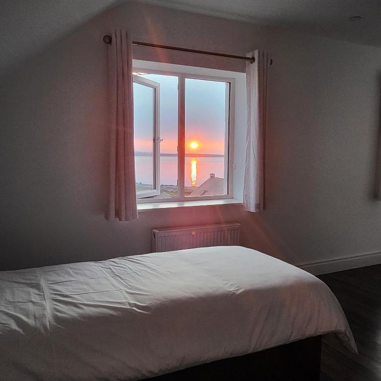 a bedroom with a bed and a window with the sunset at An Creagán Rooms in Inisheer
