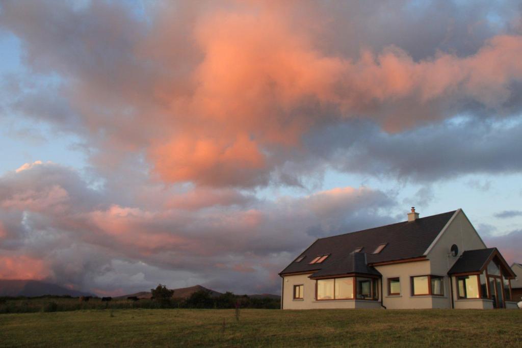 una casa in un campo sotto un cielo nuvoloso di Uisce Beatha House B&B a Portmagee