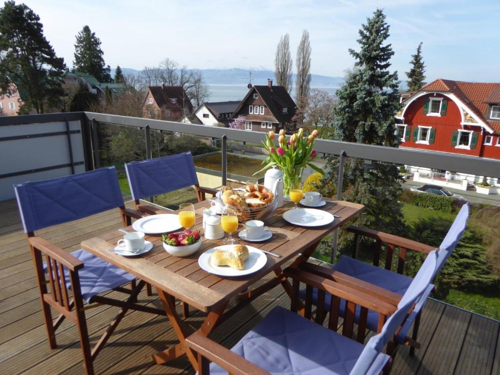 einen Holztisch mit Essen auf einem Balkon mit Stühlen in der Unterkunft Ferienwohnung Bodenseeblick in Nonnenhorn