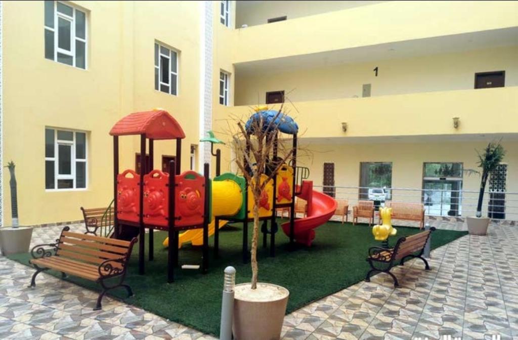 a playground with a slide and benches in front of a building at مجمع الحديقة in Salalah