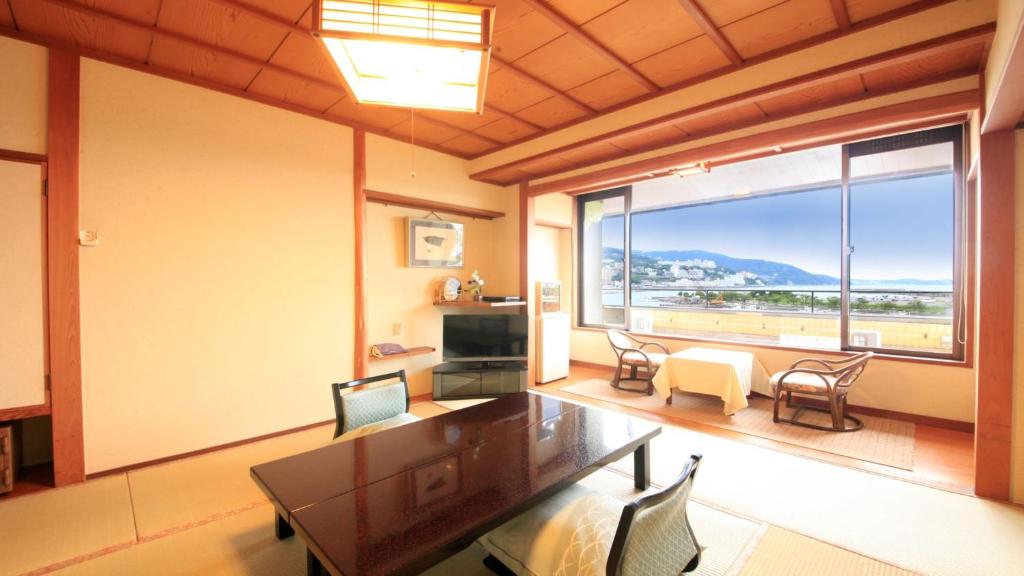 a living room with a table and chairs and a large window at Syukaen Yunohanazen in Atami