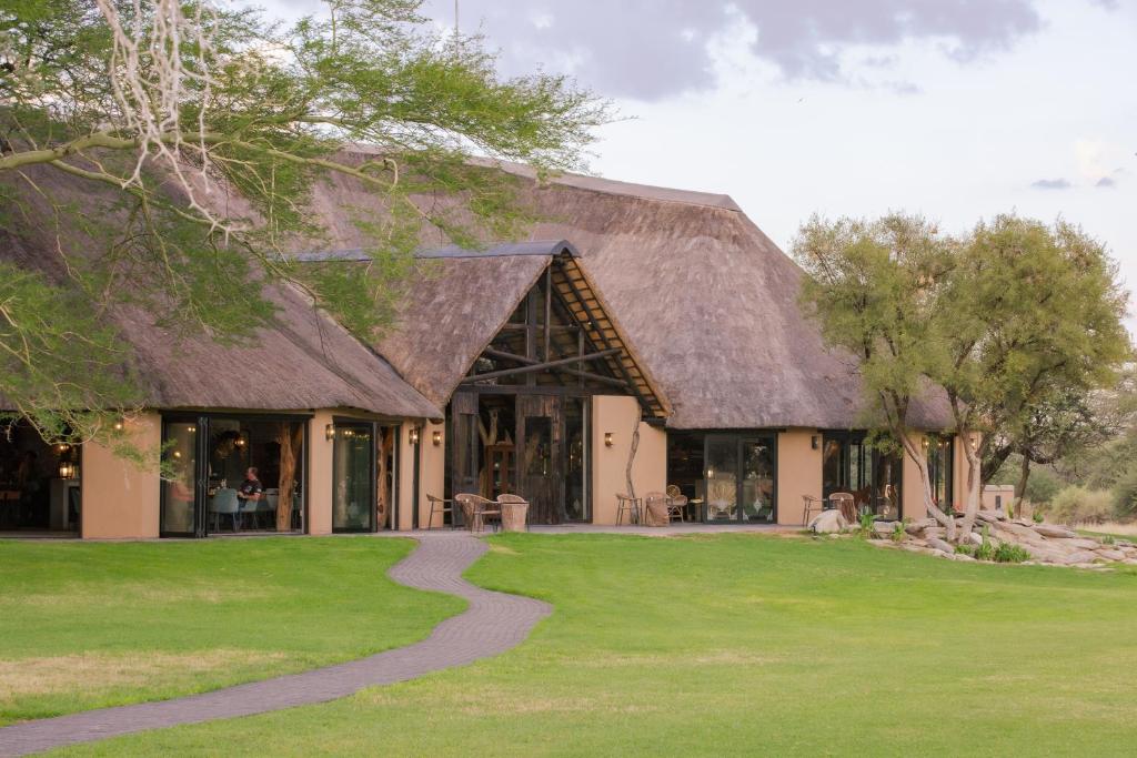 a building with a thatched roof with a path in front at Okapuka Safari Lodge in Windhoek