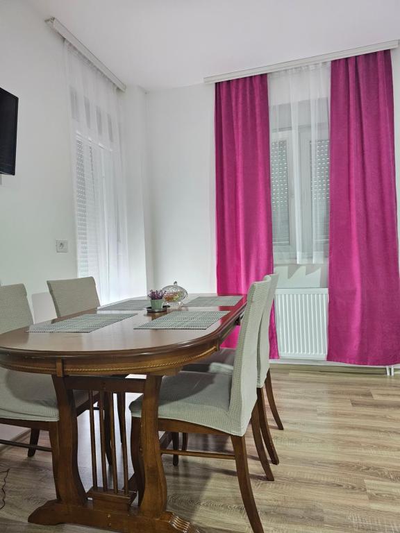 ein Esszimmer mit einem Holztisch und rosa Vorhängen in der Unterkunft AL Apartments 02 in Prizren