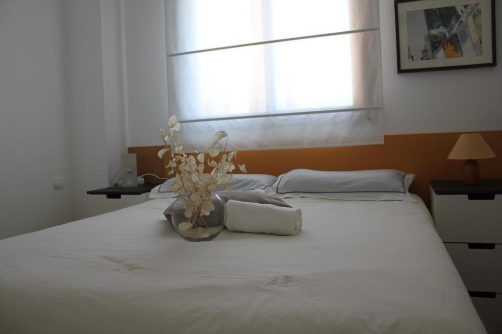 ein weißes Bett mit einer Blumenvase drauf in der Unterkunft APARTAMENTO BARAJAS-IFEMA in Madrid