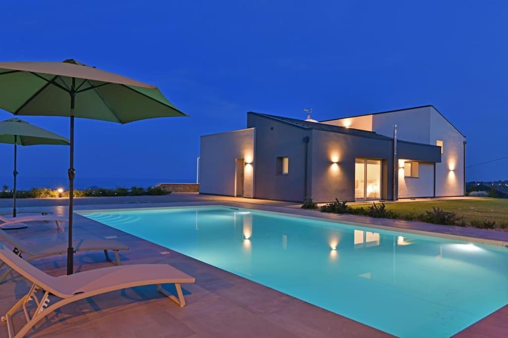 uma piscina com duas cadeiras e um guarda-sol em Modern Villa, pool + gym em Giarre
