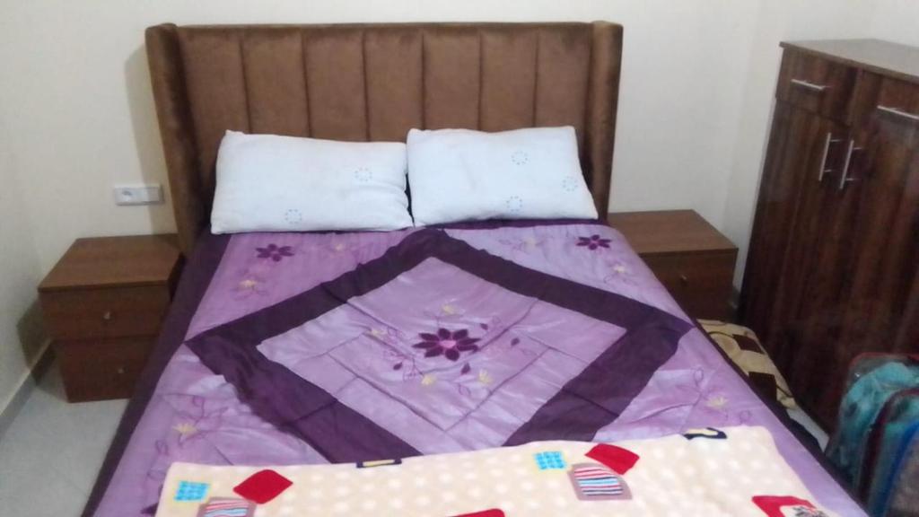 a bed with a purple comforter and two pillows at appartement pour famille in Agadir