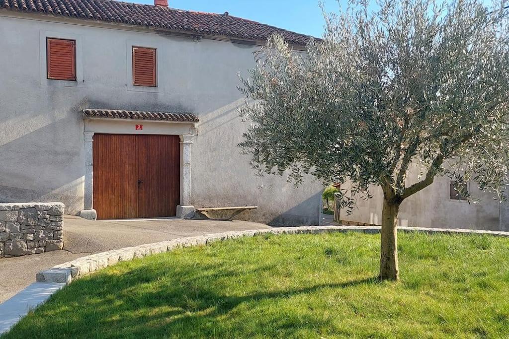 un árbol frente a una casa con garaje de madera en Sea View Karst House Apartment with Bikes, en Komen