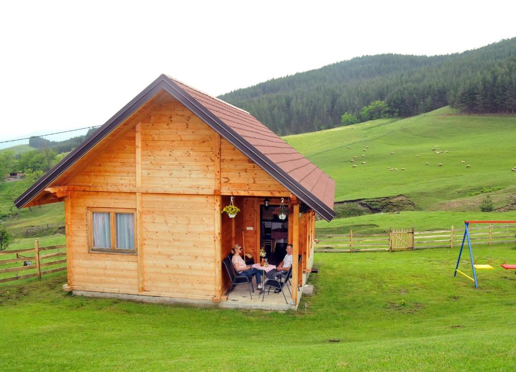 two people sitting in the doorway of a cabin in a field at Milošev vajat - Miloš's cottage in Mionica