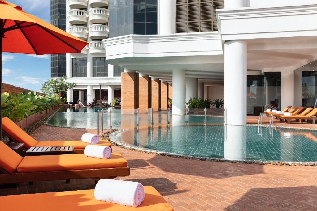 A sunlit outdoor pool deck with orange loungers beside the hotel tower.
