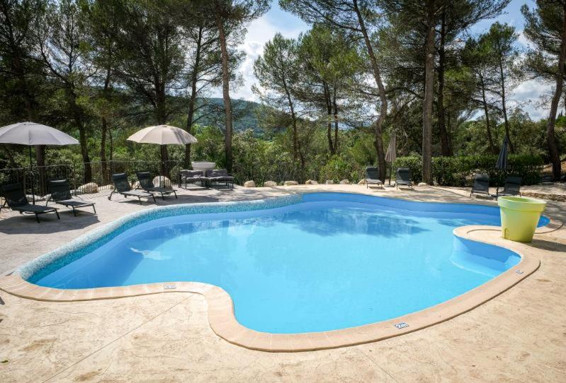 a large blue swimming pool with chairs and umbrellas at Hôtel La Pinède in Saint-Marcellin-lès-Vaison