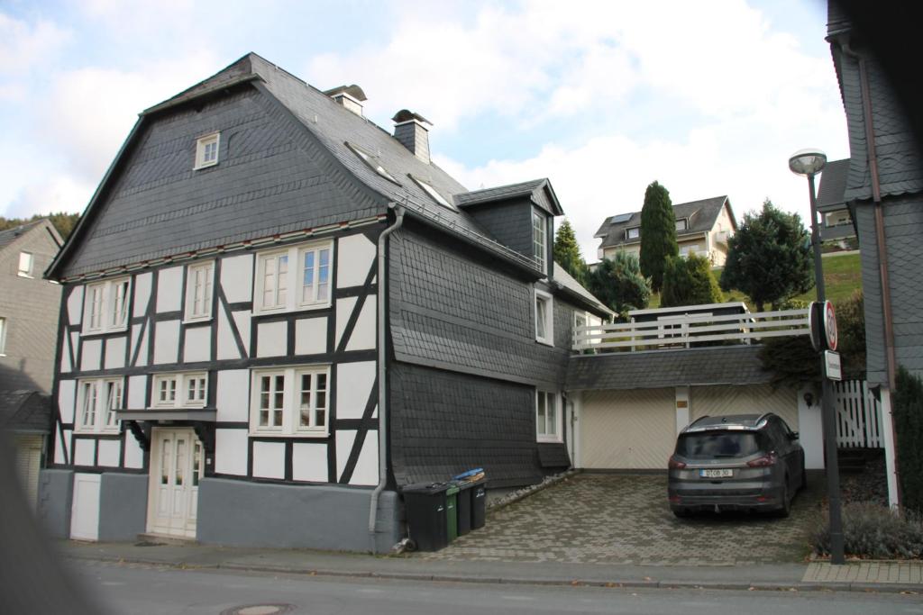 uma casa a preto e branco com um carro estacionado em frente em Ferienhaus Winterberg für 12 Personen Sauna Garten Garage Hund em Winterberg