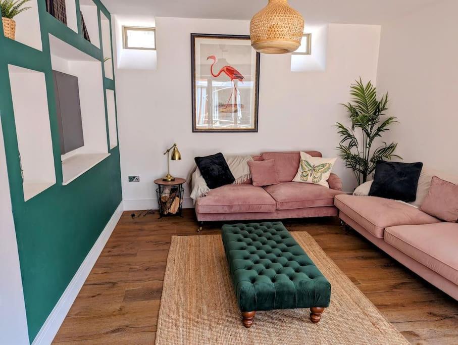 a living room with a pink couch and a green stool at The Livery Cottage at Cefn Tilla Court, Usk in Usk
