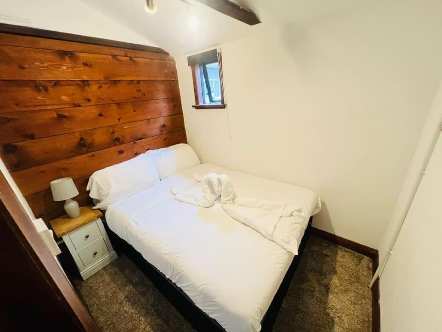 a small bedroom with a white bed with a wooden wall at The Granary in Birchington
