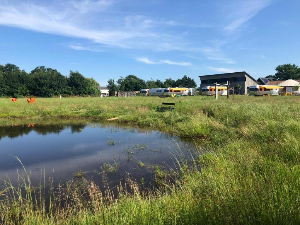 einen Teich auf einem Feld mit einem Gebäude im Hintergrund in der Unterkunft Rusttheater, genieten van rust en ruimte in Reutum