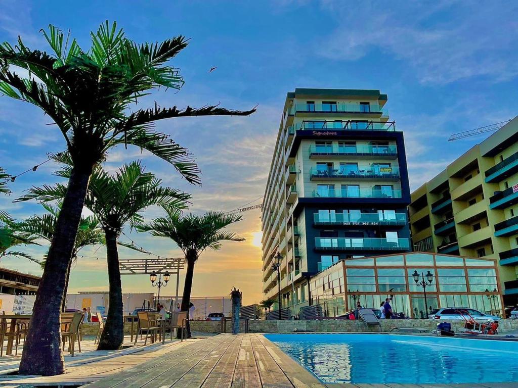 a building and palm trees next to a swimming pool at Signature PROMENADA Hotel Apartments in Mamaia Nord