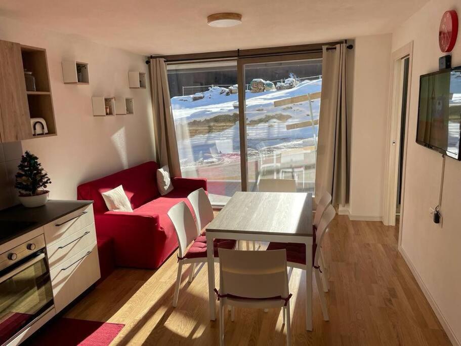 a living room with a table and a red couch at Appartamento nuovo tra Bormio e Livigno in Valdidentro