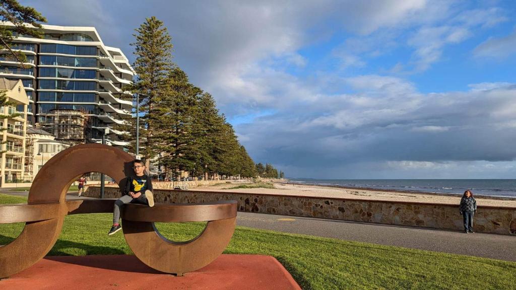 a man sitting on a bench next to the beach at Glenelg resort style beachside apartment in Glenelg
