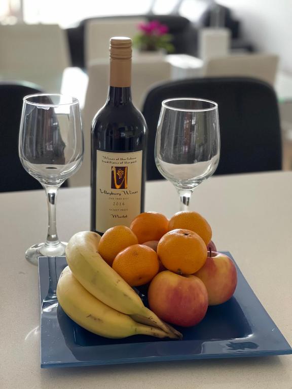 a plate of fruit with a bottle of wine and two glasses at Glenelg resort style beachside apartment in Glenelg